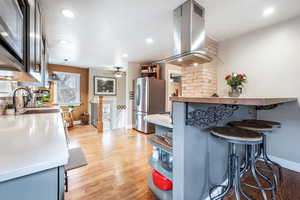 Kitchen featuring light wood-style floors, freestanding refrigerator, light countertops, and island range hood