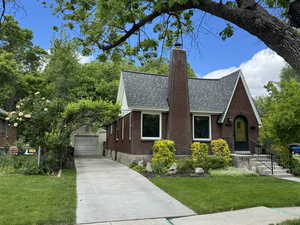 Tudor house with a shingled roof, a chimney, an outdoor structure, a front lawn, and brick siding