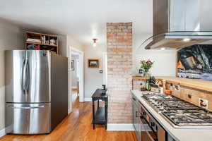 Kitchen with light wood finished floors, tasteful backsplash, baseboards, island exhaust hood, and stainless steel appliances