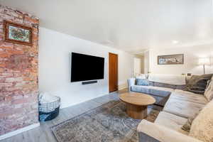 Living area featuring brick wall, baseboards, visible vents, and wood finished floors