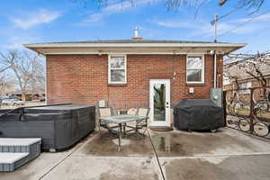 Back of house with a patio area, a hot tub, outdoor dining space, and brick siding