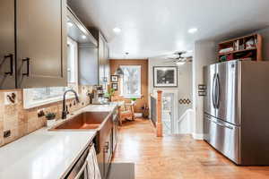 Kitchen featuring light wood-style flooring, light countertops, freestanding refrigerator, tasteful backsplash, and decorative light fixtures