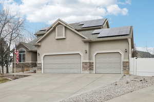 View of front facade featuring an attached garage, solar panels, fence, stone siding, and stucco siding