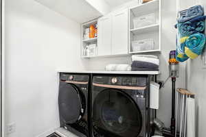 Washroom featuring washing machine and clothes dryer, cabinet space, and baseboards