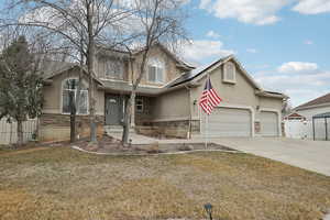 View of front of property featuring driveway, solar panels, stone siding, fence, and stucco siding