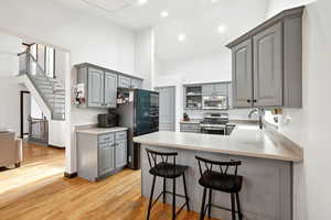 Kitchen featuring gray cabinets, stainless steel appliances, light countertops, light wood-type flooring, and a sink