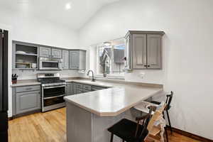 Kitchen with appliances with stainless steel finishes, a peninsula, gray cabinets, light countertops, and open shelves