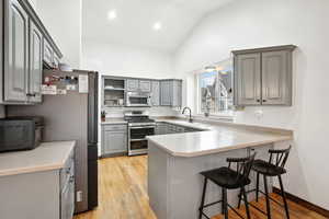 Kitchen with appliances with stainless steel finishes, a sink, a peninsula, and gray cabinetry