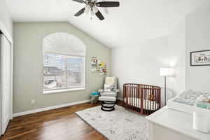 Bedroom featuring a crib, baseboards, a ceiling fan, lofted ceiling, and dark wood-style floors