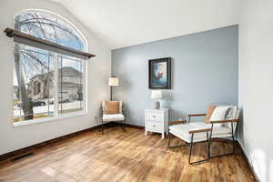 Sitting room with lofted ceiling, baseboards, visible vents, and wood finished floors