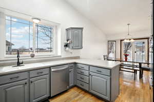 Kitchen with a peninsula, a sink, light countertops, stainless steel dishwasher, and gray cabinets