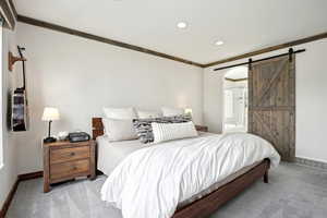 Bedroom featuring light carpet, a barn door, baseboards, connected bathroom, and ornamental molding