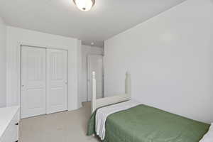 Bedroom featuring a closet, light colored carpet, and a textured ceiling