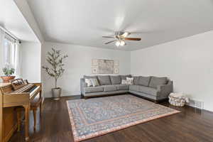 Living area featuring a ceiling fan, baseboards, visible vents, and dark wood-type flooring