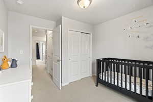 Bedroom with a nursery area, a closet, light carpet, and a textured ceiling