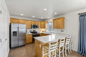 Kitchen with stainless steel appliances, a peninsula, a sink, a kitchen breakfast bar, and light countertops