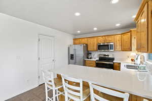 Kitchen with stainless steel appliances, a peninsula, a sink, a kitchen breakfast bar, and light countertops