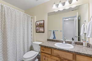 Full bath with curtained shower, visible vents, vanity, and toilet