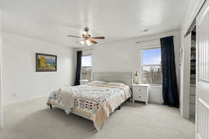 Bedroom featuring multiple windows, visible vents, a ceiling fan, and light colored carpet