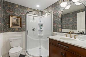 Full bathroom featuring toilet, wallpapered walls, and a wainscoted wall