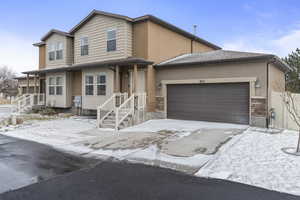 View of front of house with a garage, stone siding, concrete driveway, and stucco siding