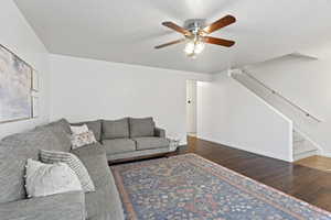 Living room featuring baseboards, a ceiling fan, dark wood-type flooring, stairs, and a textured ceiling