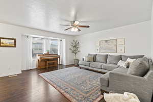 Living area featuring a ceiling fan, dark wood-style flooring, a textured ceiling, and baseboards