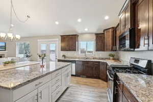 Kitchen featuring light stone countertops, stainless steel appliances, white cabinetry, and a sink