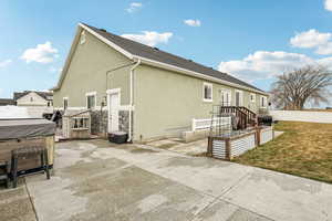 Rear view of house featuring a patio, fence, a lawn, stucco siding, and a hot tub