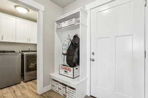 Laundry area featuring light wood-style floors, baseboards, cabinet space, and washing machine and clothes dryer