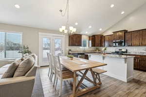 Kitchen with hanging light fixtures, light stone counters, dark brown cabinets, a kitchen island, and stainless steel appliances