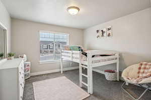 Bedroom featuring a textured ceiling, dark colored carpet, and baseboards