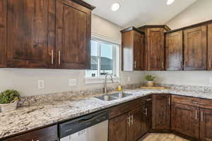 Kitchen featuring stainless steel dishwasher, light stone countertops, a sink, light wood finished floors, and vaulted ceiling