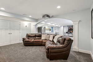 Living area with decorative columns, arched walkways, dark colored carpet, and recessed lighting