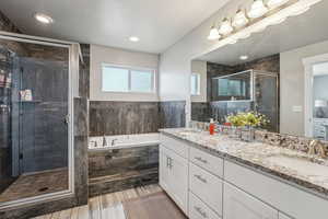 Bathroom featuring a bath, a shower stall, double vanity, and a sink