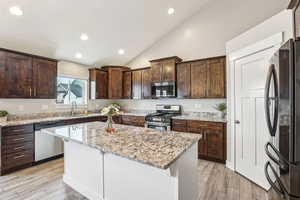 Kitchen featuring a sink, a kitchen island, light stone counters, appliances with stainless steel finishes, and wood finish floors