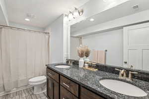 Bathroom with double vanity, visible vents, toilet, and a sink