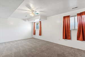 Carpeted spare room with a healthy amount of sunlight, visible vents, and a textured ceiling