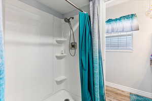 Bathroom featuring a stall shower, wood finished floors, and baseboards