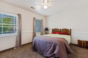 Carpeted bedroom with a wainscoted wall, visible vents, and a ceiling fan