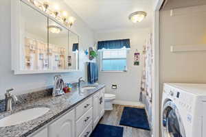 Full bathroom featuring washer / clothes dryer, double vanity, a sink, and wood finished floors