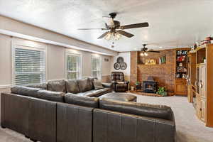 Living room with a ceiling fan, a wood stove, carpet flooring, and a textured ceiling