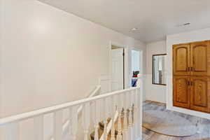 Hallway featuring a wainscoted wall, visible vents, an upstairs landing, and wood finished floors