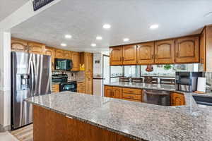 Kitchen with black appliances, light stone counters, and brown cabinets