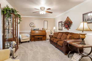 Living room featuring ceiling fan, crown molding, and light colored carpet