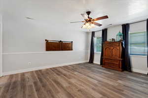 Unfurnished bedroom featuring a ceiling fan, visible vents, baseboards, and wood finished floors