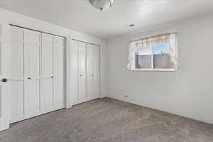 Unfurnished bedroom with carpet, a textured ceiling, visible vents, and multiple closets