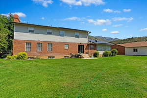 Back of house featuring brick siding, a chimney, a lawn, central AC unit, and a mountain view