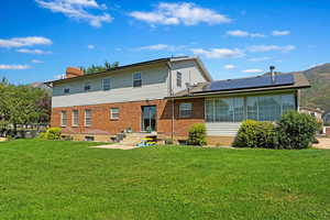 Back of house with brick siding, a yard, a chimney, and solar panels