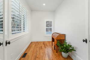 Hallway featuring light wood finished floors, baseboards, visible vents, and a wealth of natural light